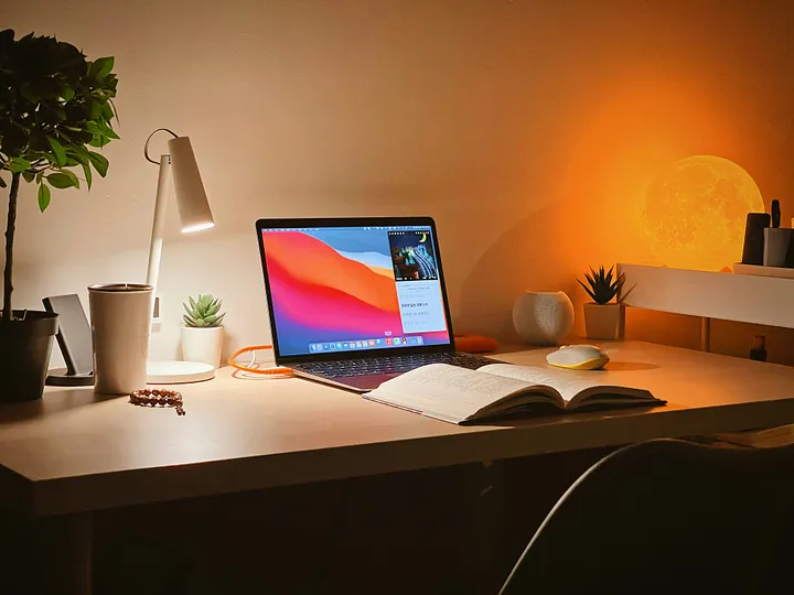 A cozy study desk with a laptop, book, and warm lighting.